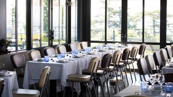 A dining area with tables set for multiple guests, large windows, and a view of the outdoors.