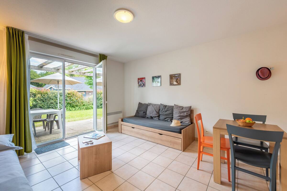 Una sala de estar moderna con un sofá, una mesa de comedor y sillas. Hay una puerta corrediza de vidrio que da a un patio.