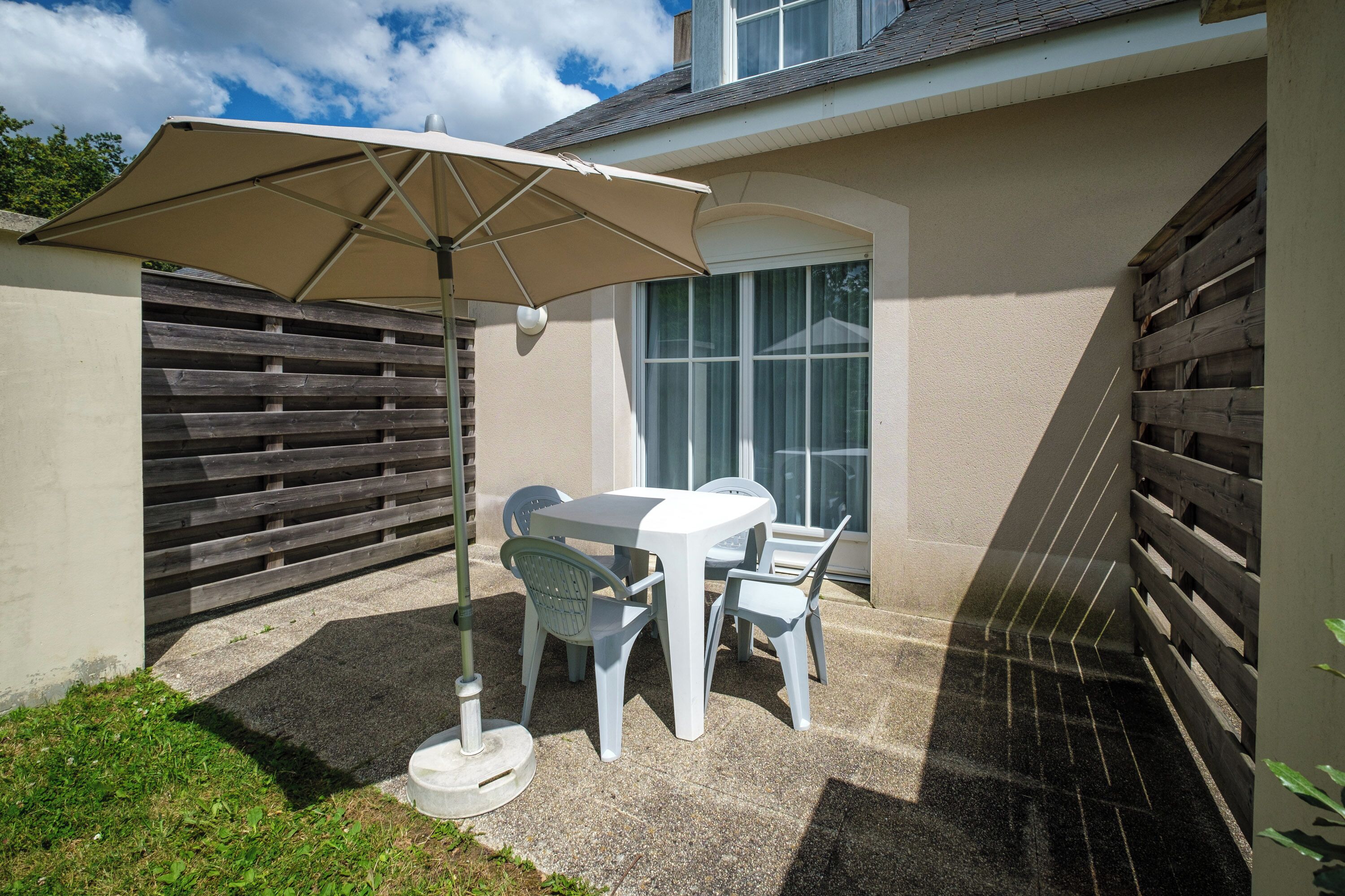 A patio with a table and chairs, a beige umbrella, and a wooden fence.