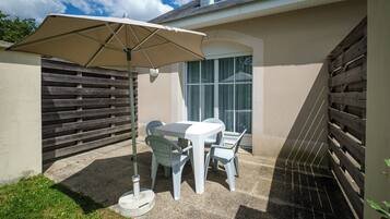 A patio with a table and chairs, a beige umbrella, and a wooden fence.