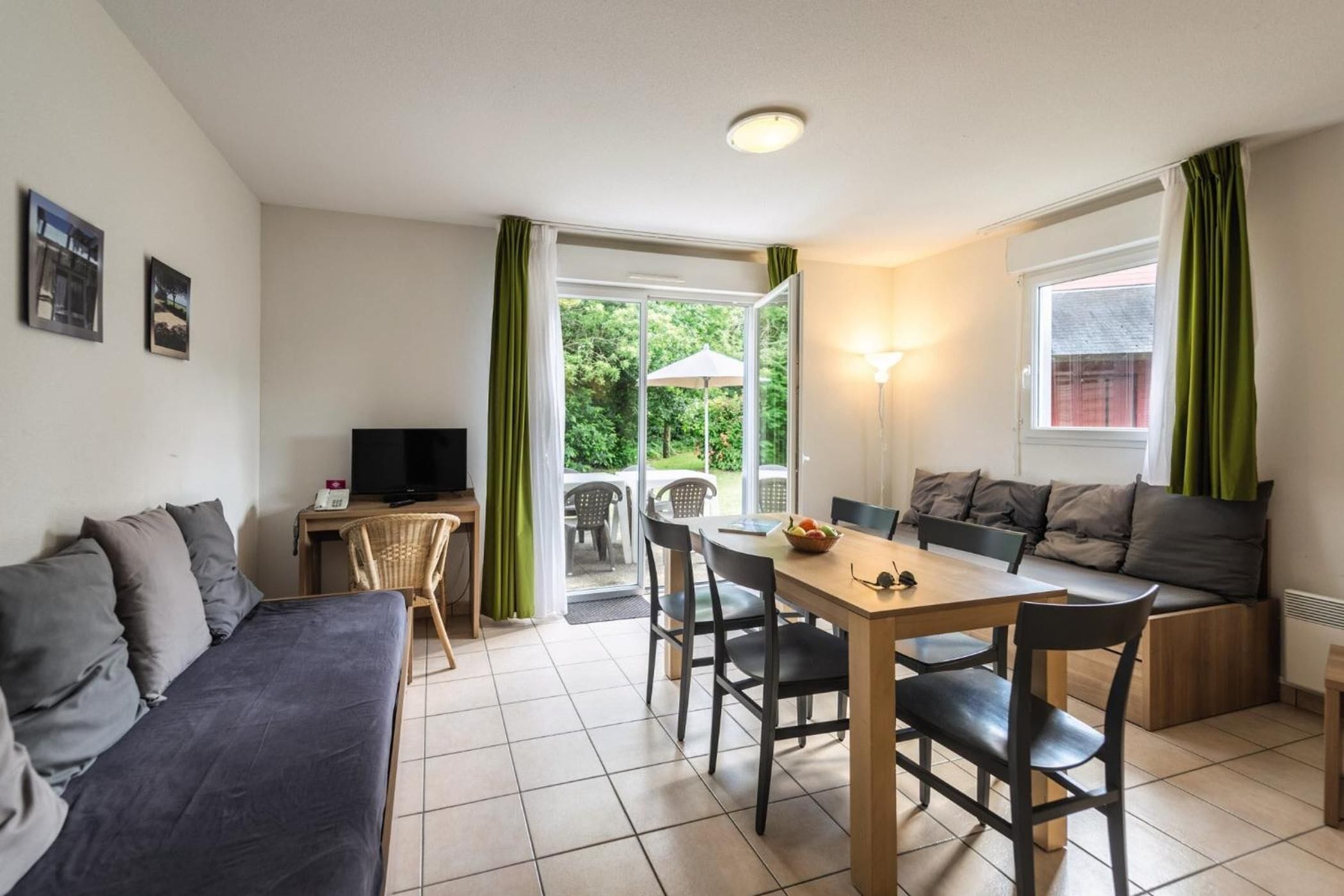 A room with a sofa, a dining table with chairs, a TV, and a window with curtains.