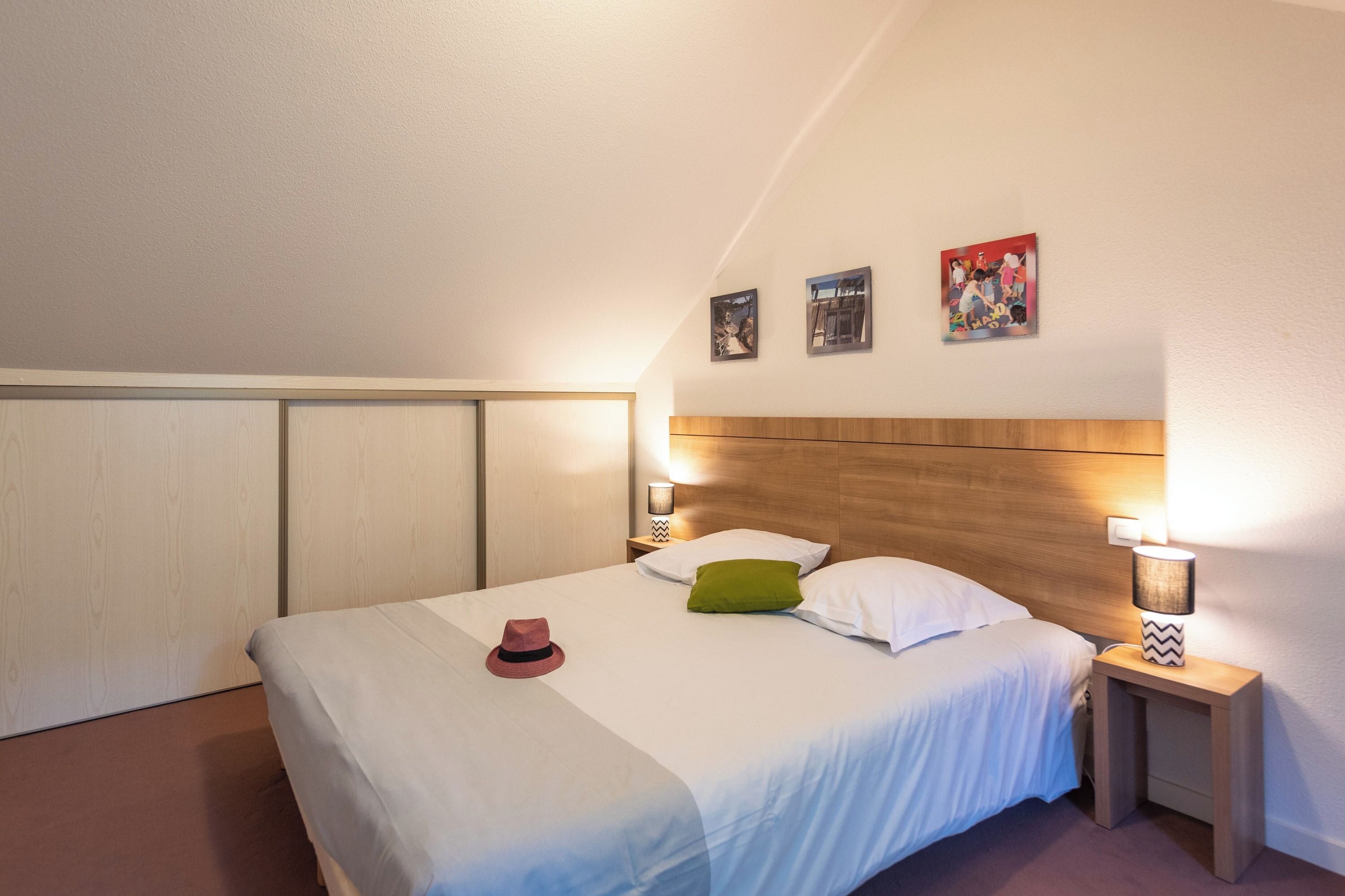 A neatly made bed with a hat, pillows, and a nightstand with a lamp.