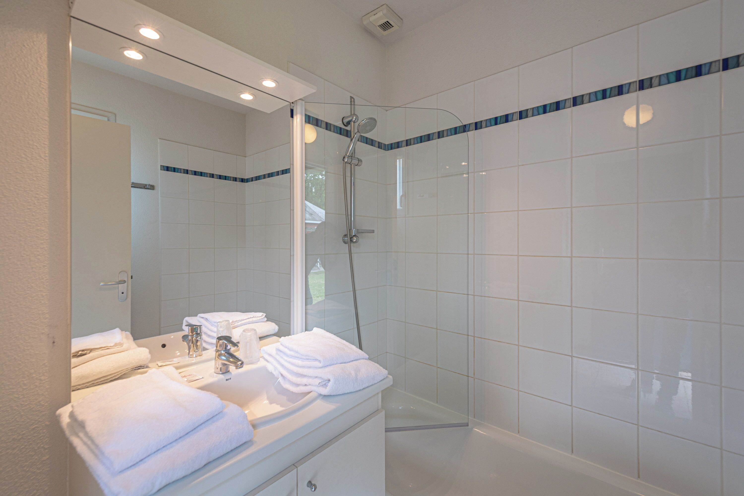 A modern bathroom with a glass-enclosed shower, white tiles, and neatly folded towels on the vanity.