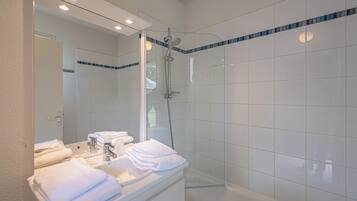 A modern bathroom with a glass-enclosed shower, white tiles, and neatly folded towels on the vanity.