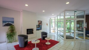 Eine Lobby mit rotem Teppich, zwei Sessel, einem kleinen Tisch, einem Fernseher und einer Glastür zum Ausgang.