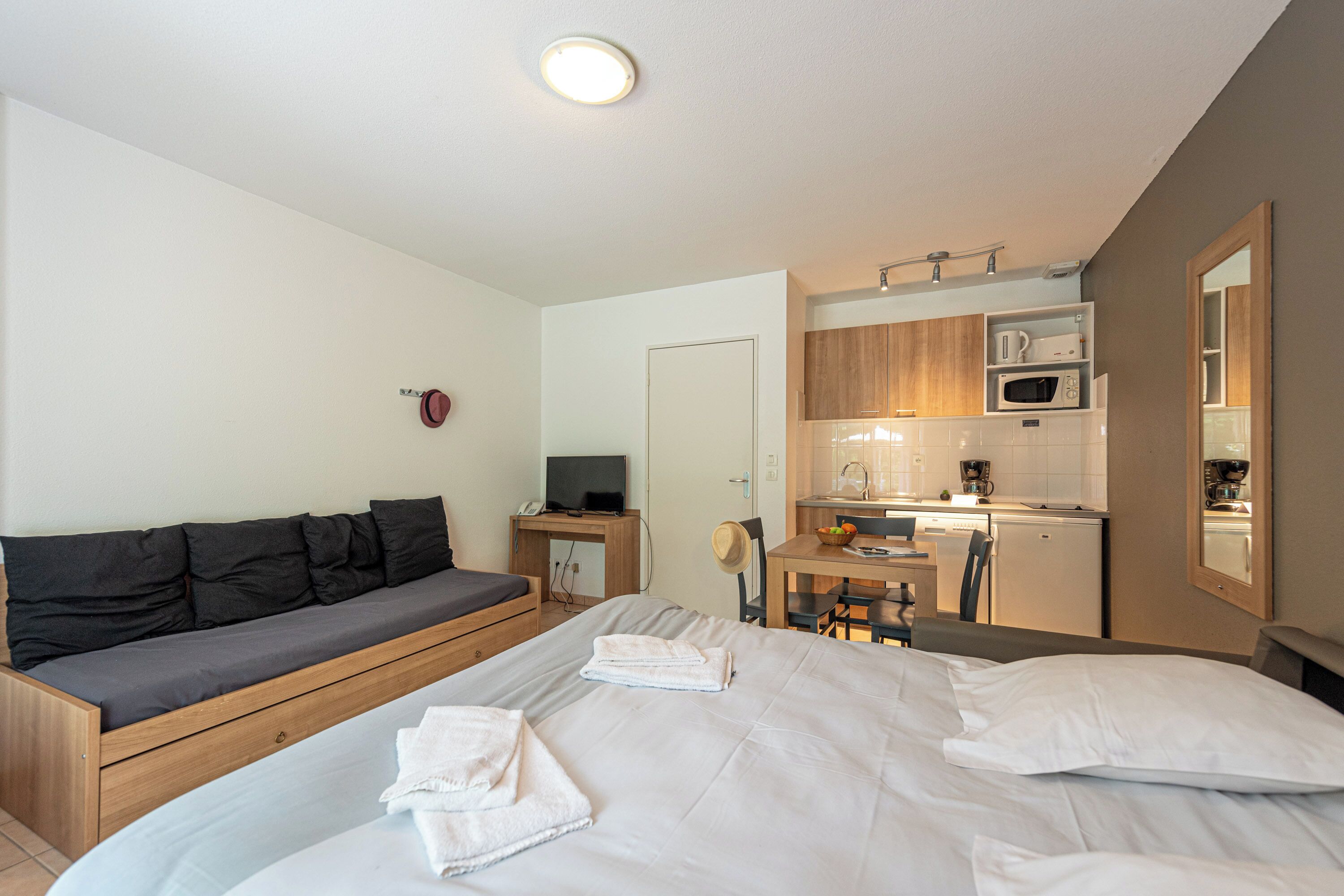 A compact hotel room with a bed, a sofa, a small kitchenette, and a dining area.
