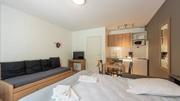 A compact hotel room with a bed, a sofa, a small kitchenette, and a dining area.