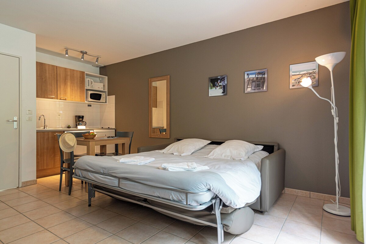 Ett kompakt hotellrum med en säng, ett litet pentry, en matplats och ett badrum.