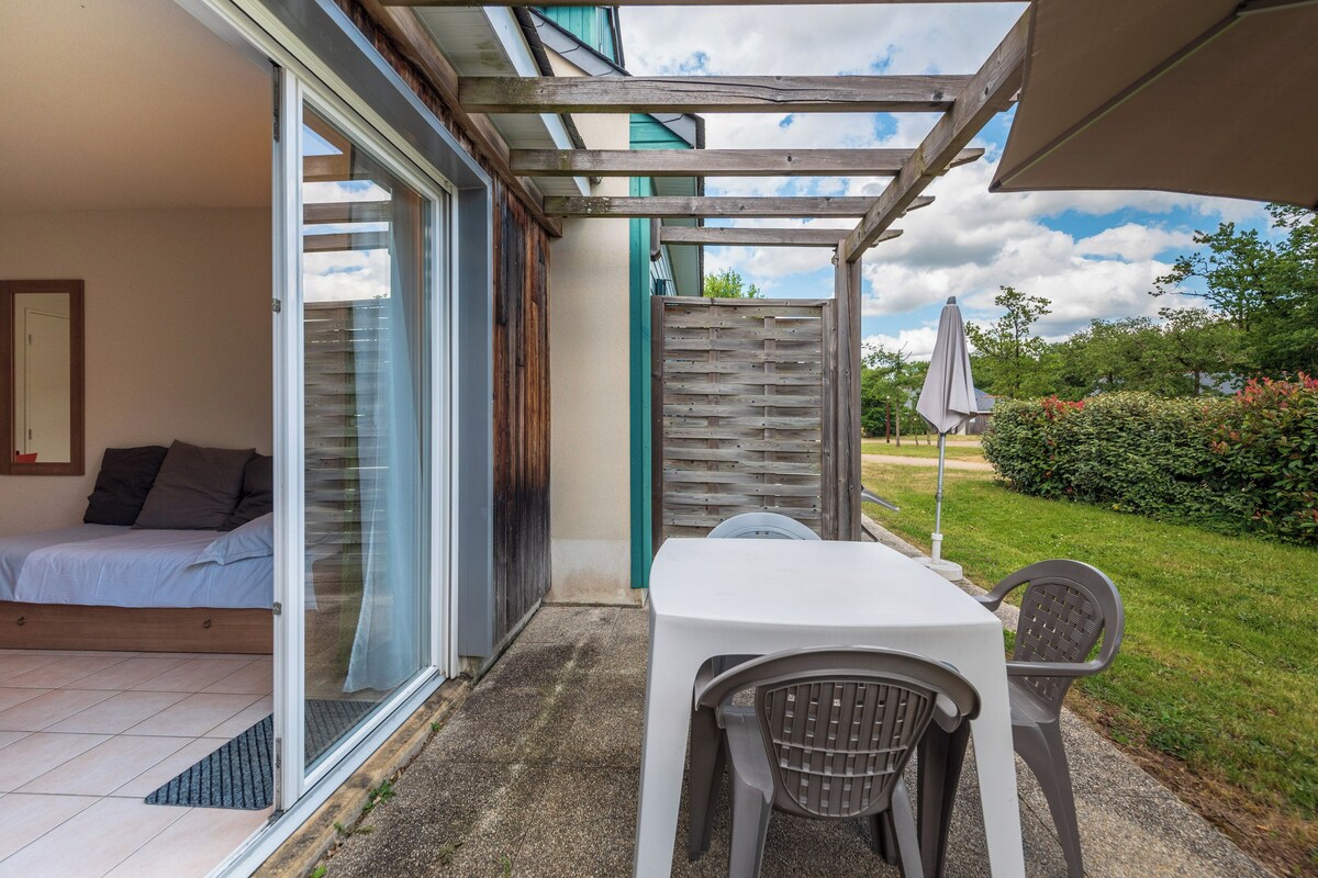 A bedroom with a sliding glass door leading to a patio with a table and chairs, a bed, and a view of the garden.