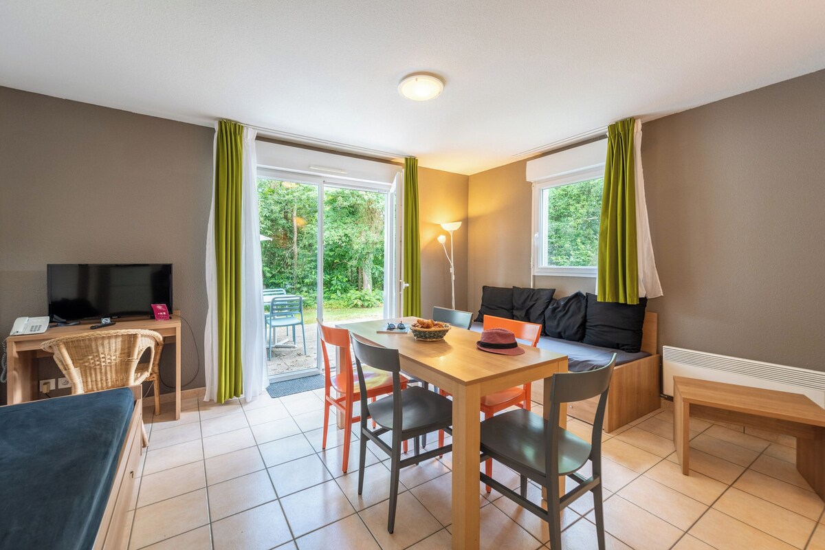 A room with a bed, a desk with a TV, a dining table with chairs, a sofa, and a lamp.