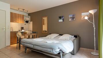 Habitación de hotel compacta con cama, kitchenette pequeña, zona de comedor y baño.