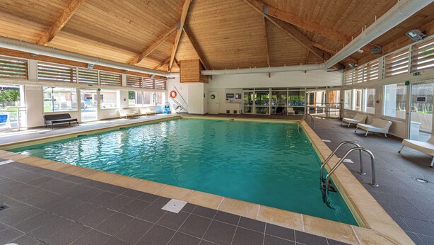 Ein Innenpool mit Holzbalkendecke, Fliesenboden und einem Rettungsschwimmerstuhl.
