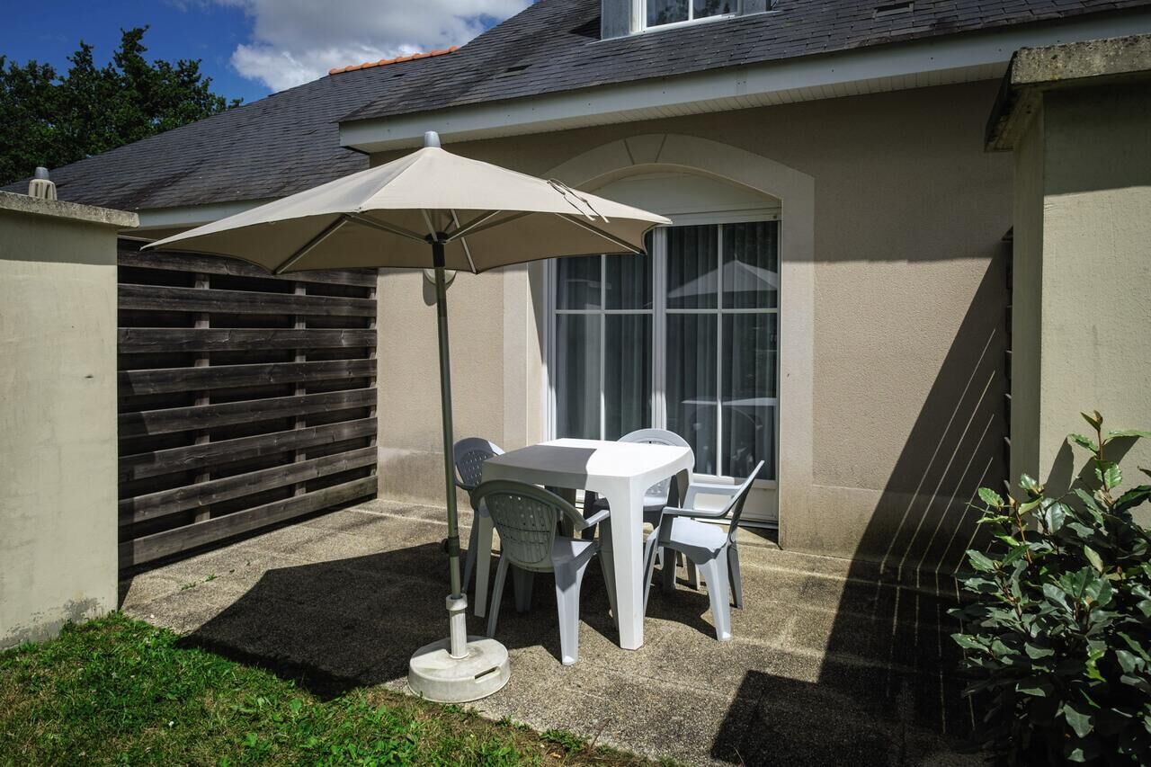 Een terras met een tafel en stoelen onder een luifel, een houten hek en een gebouw met een raam.