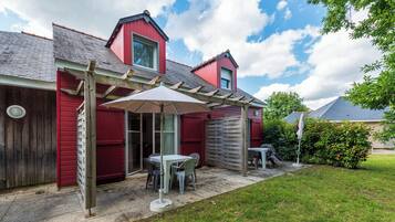 A red building with a covered patio area, a wooden pergola, and a small table with chairs.