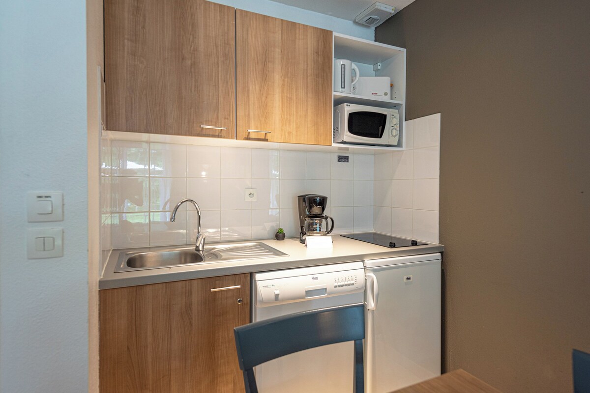 A compact kitchen with wooden cabinets, a microwave, a coffee maker, and a dishwasher.