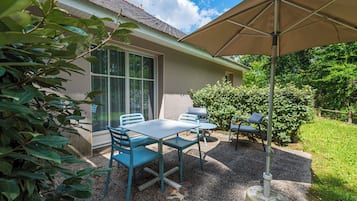 An outdoor patio with a table and chairs, a large umbrella, and a house in the background.