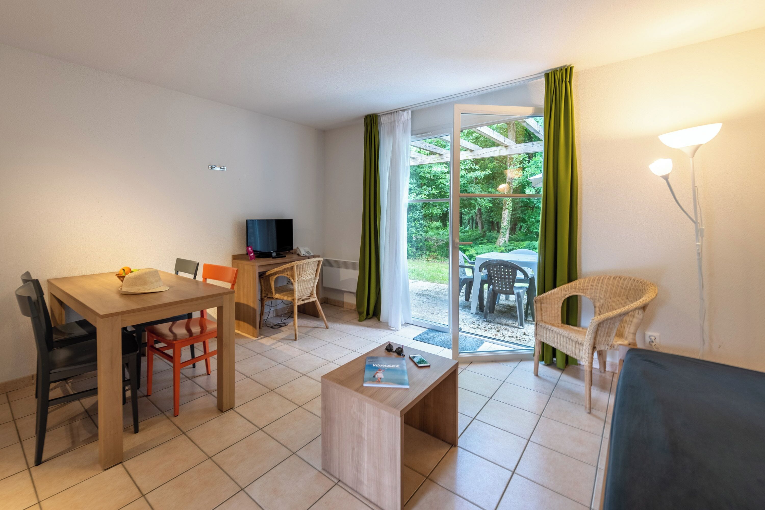 A furnished room with a dining table, chairs, a sofa, a TV, and a window with curtains.