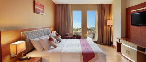 A hotel room with a large bed, a television, a desk, and a view of the city.