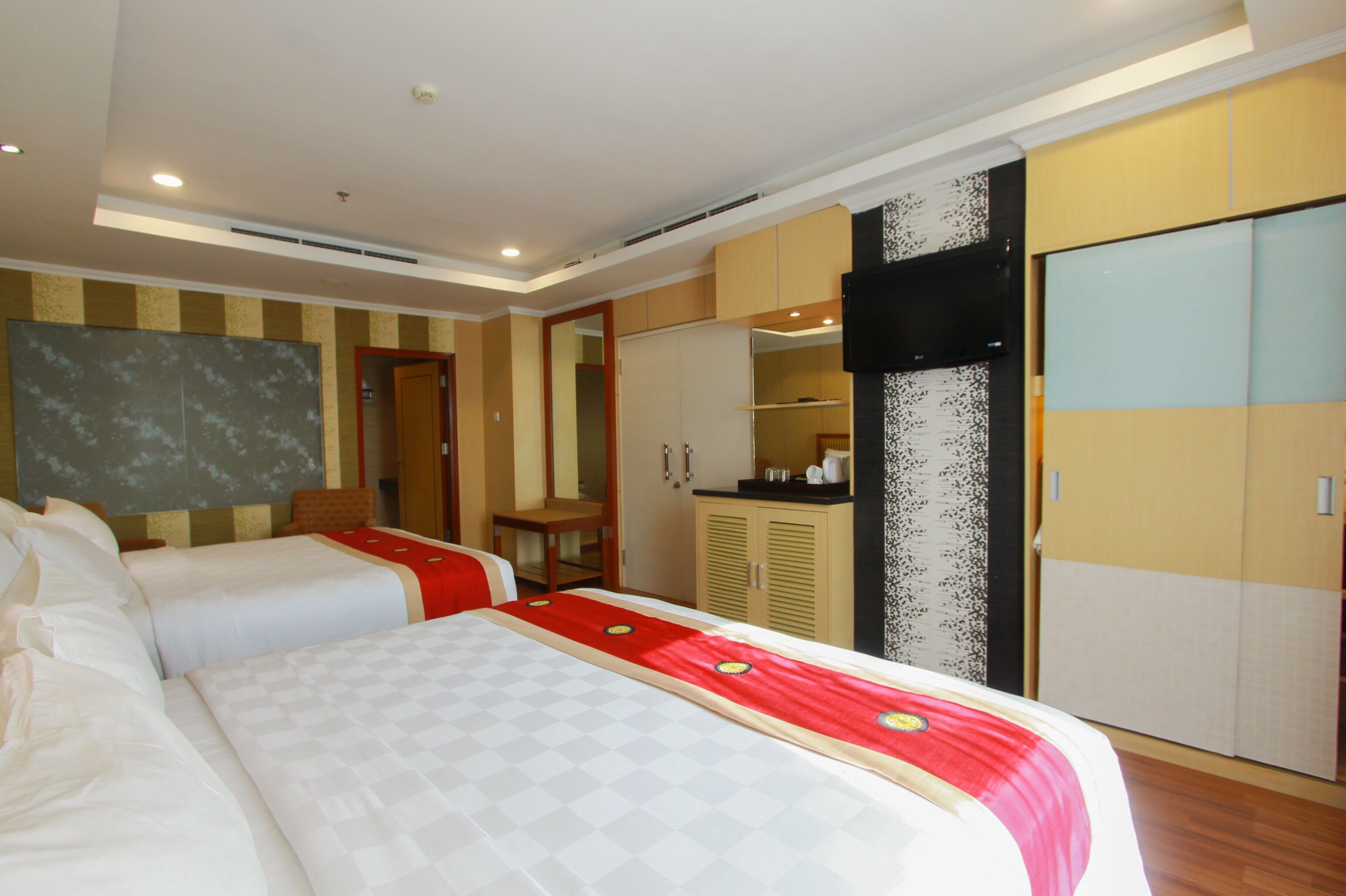A hotel room with two beds, a wardrobe, a mirror, and a small kitchenette.