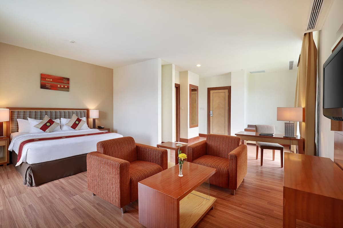 Una habitación de hotel con una cama, dos sofás, una mesa de centro, un escritorio y un televisor.