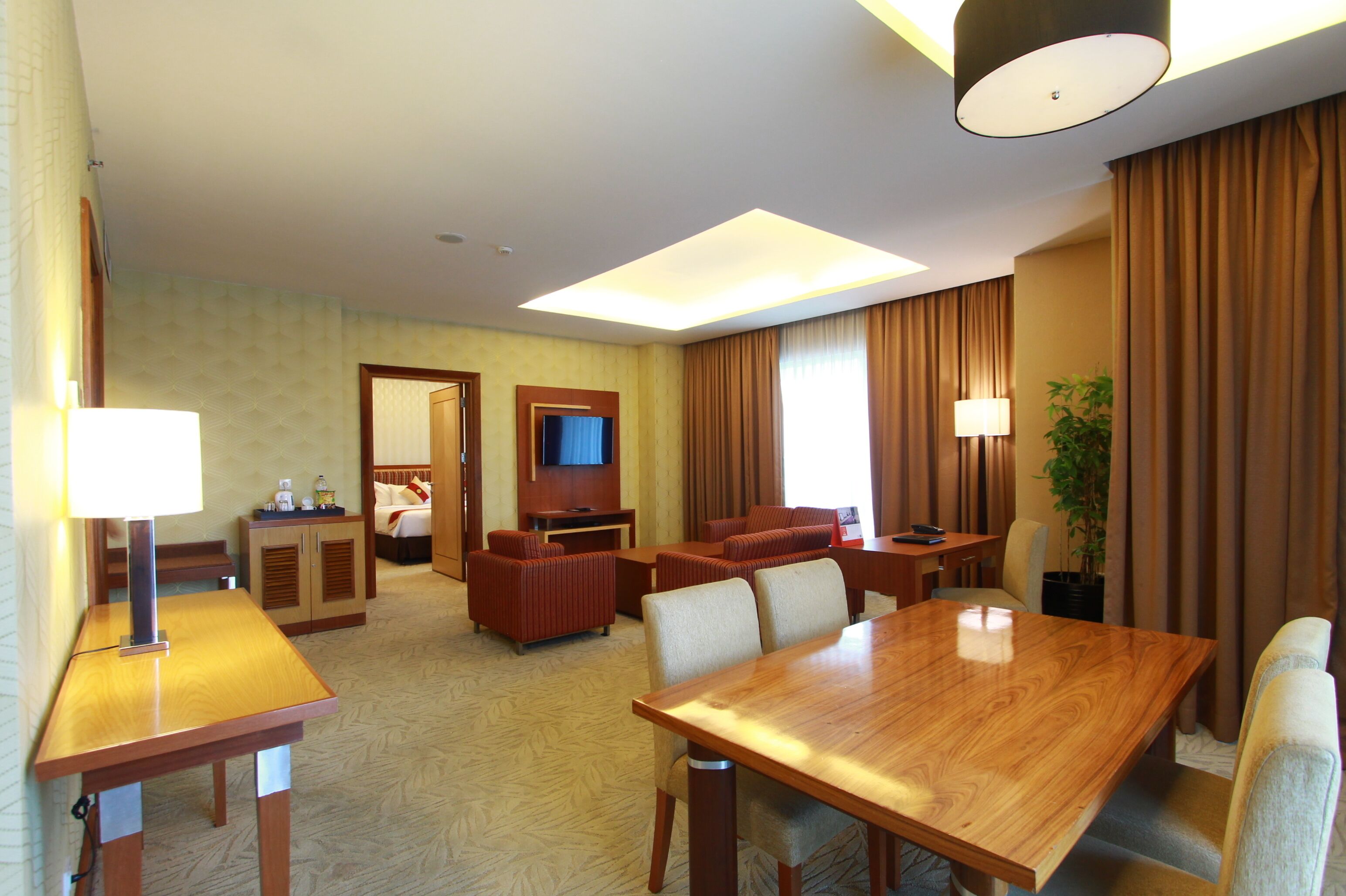 A hotel room with a wooden dining table, two sofas, a TV, and a plant.
