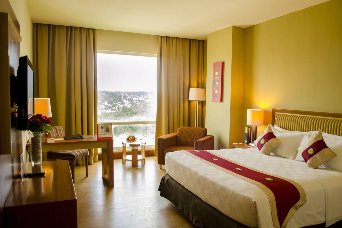 Habitación de hotel con una cama grande, un escritorio, una silla, una mesita y vistas al exterior.