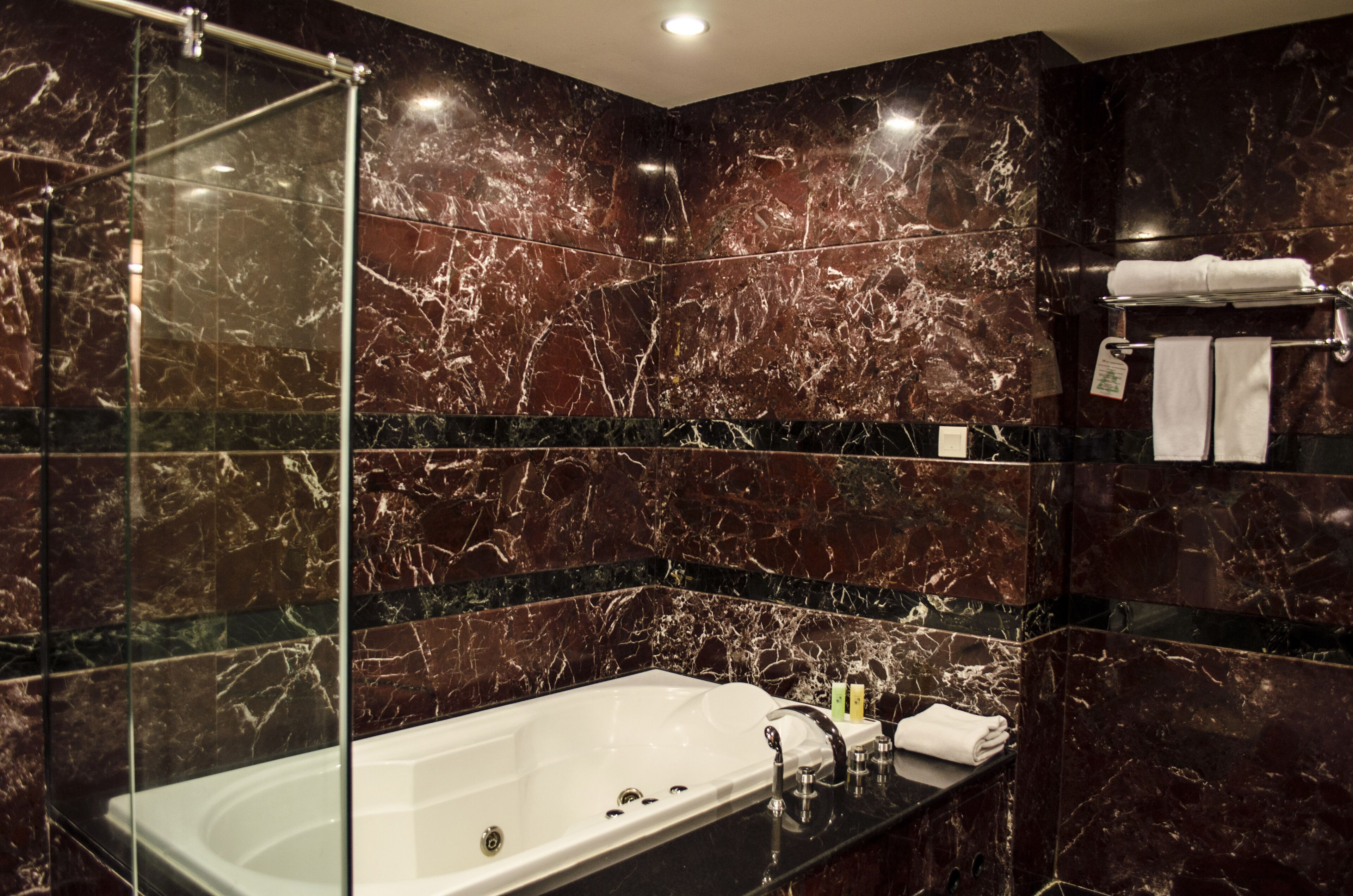 A modern bathroom with a glass-enclosed shower, a white bathtub, and marble walls.