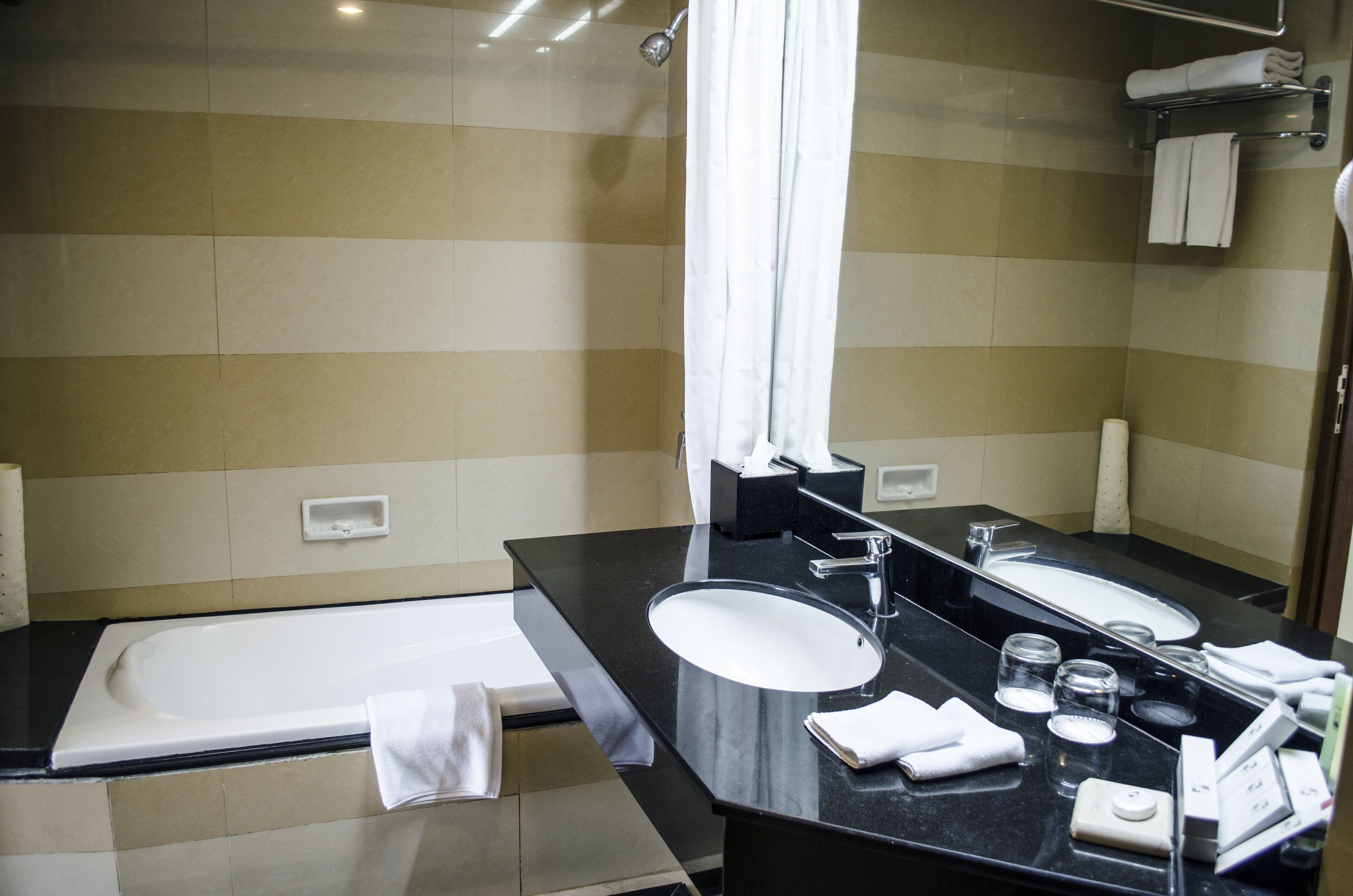 Une salle de bain moderne avec un plan de toilette noir, un lavabo blanc, un grand miroir, une baignoire et un rideau de douche.