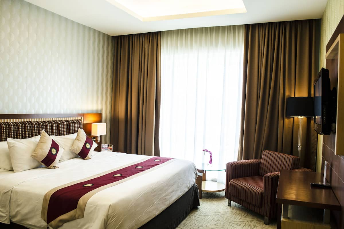 Habitación de hotel con una cama grande, un escritorio, una silla, un televisor y una ventana con cortinas.