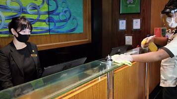 A hotel reception area with a receptionist behind a glass counter, a laptop, and a decorative wall painting.