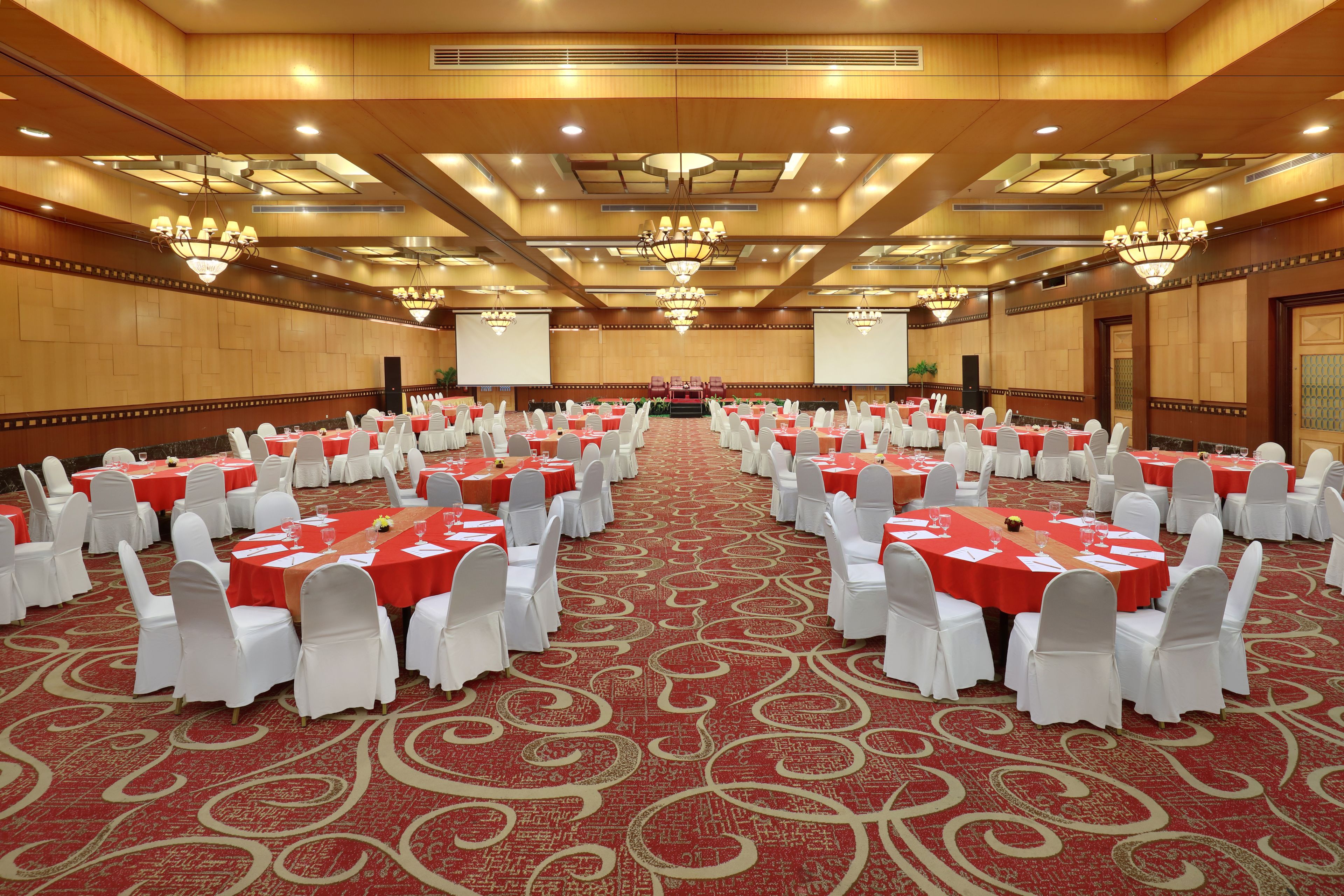 A large conference room with rows of tables and chairs, a red carpet, and chandeliers.