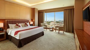 A hotel room with a large bed, a TV, a desk, and a view of the city.