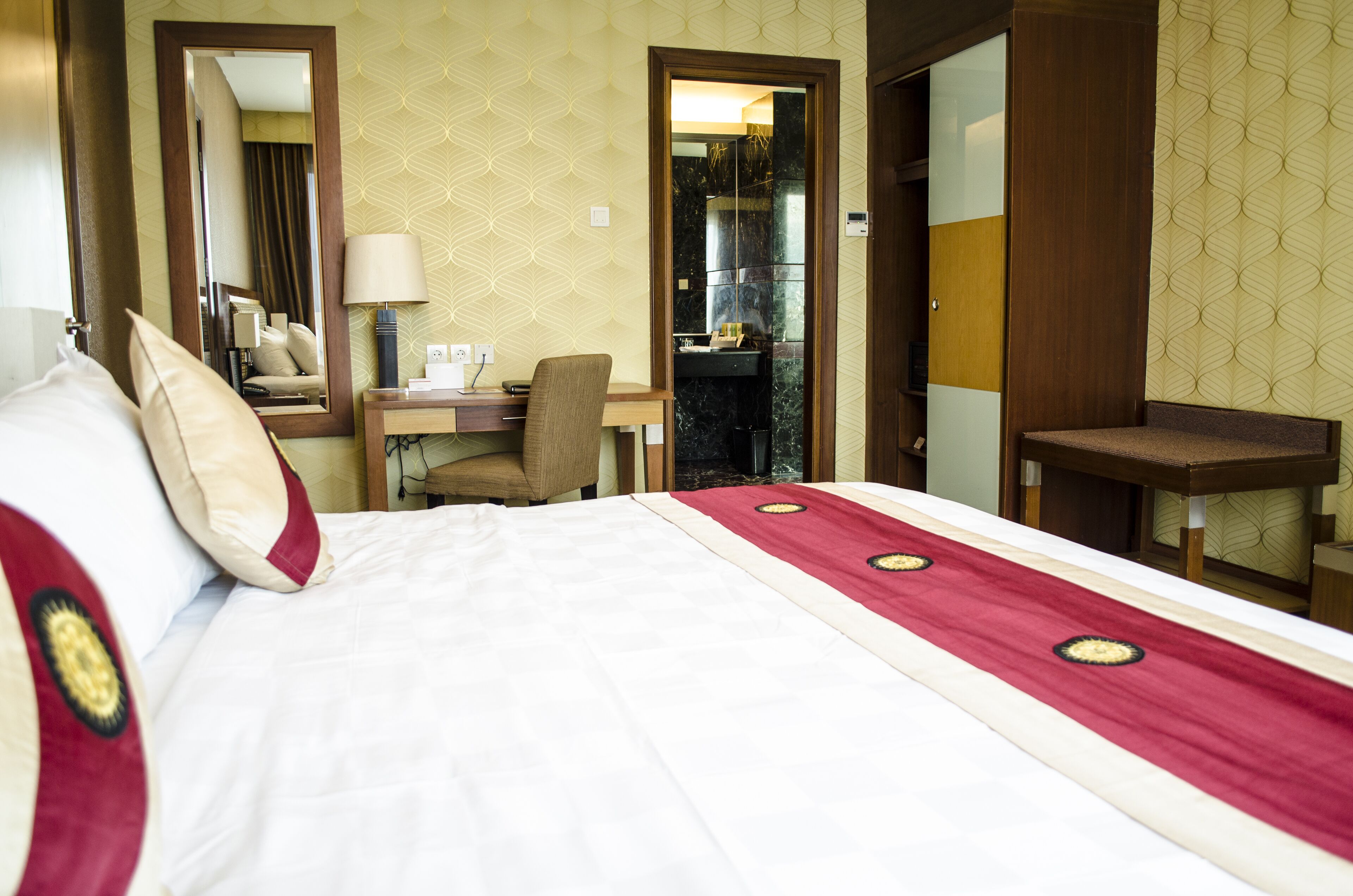A hotel room with a bed, a desk, a chair, a mirror, and a bathroom visible through an open door.