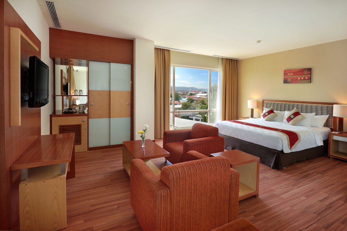 A hotel room with a bed, a desk, a chair, a TV, and a large window with a city view.