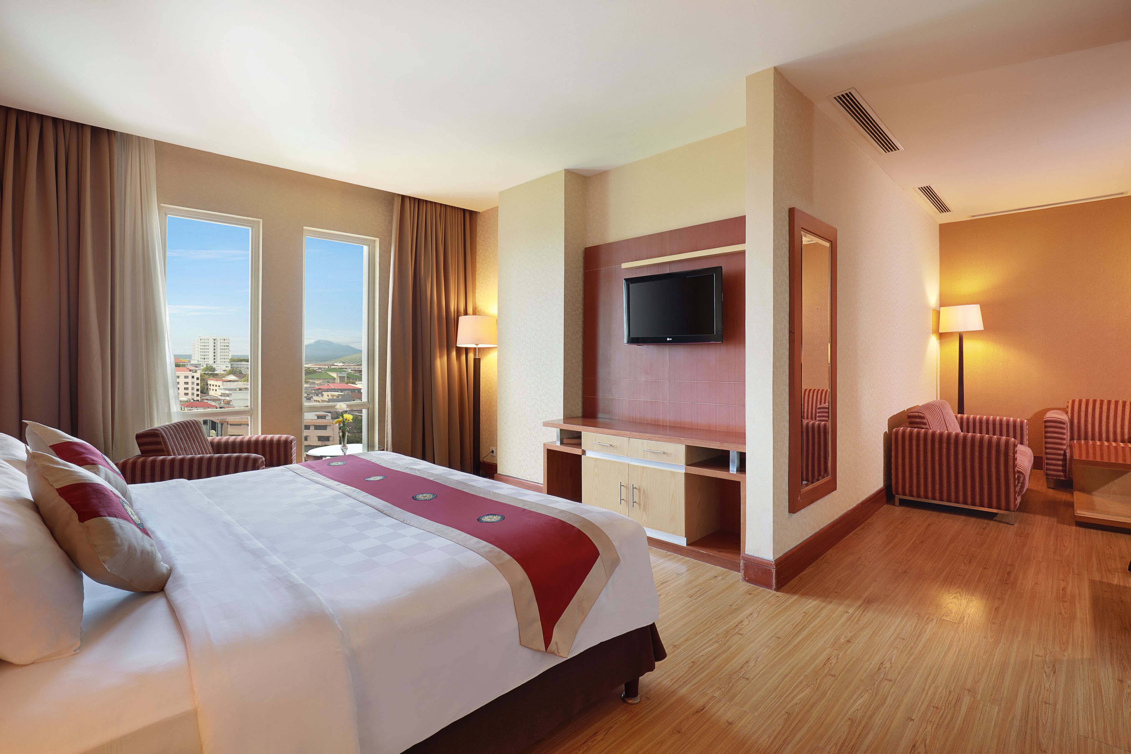 A hotel room with a large bed, a TV mounted on the wall, a desk with a chair, and a seating area with chairs.