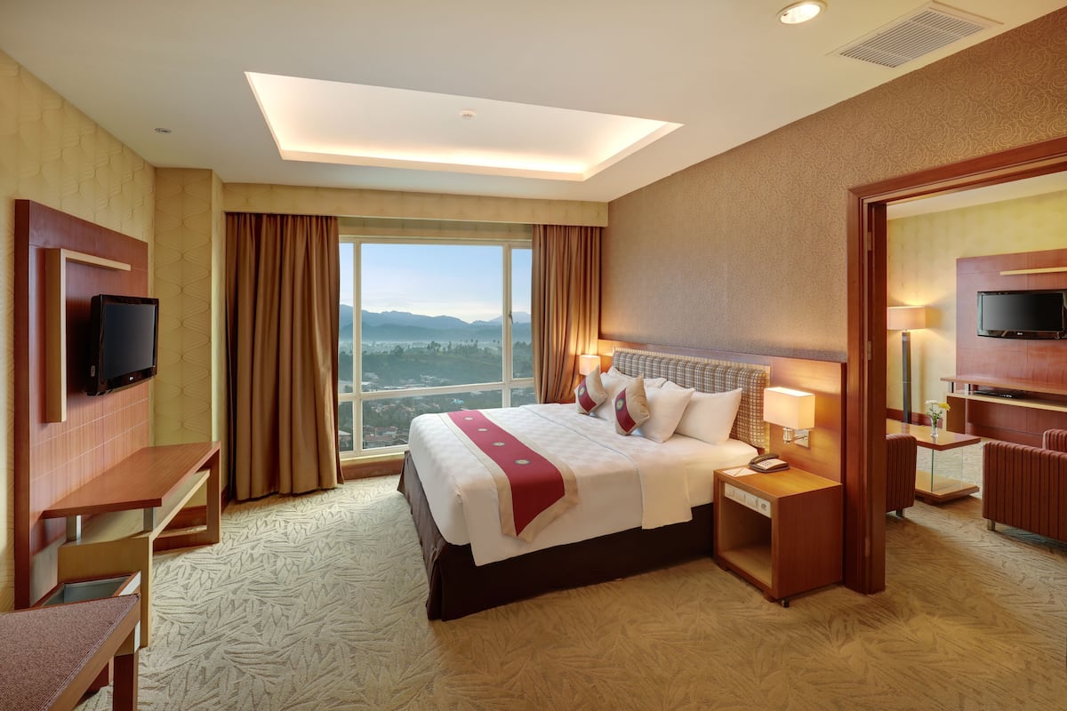 Habitación de hotel con una cama grande, un escritorio, un televisor y vistas a las montañas.