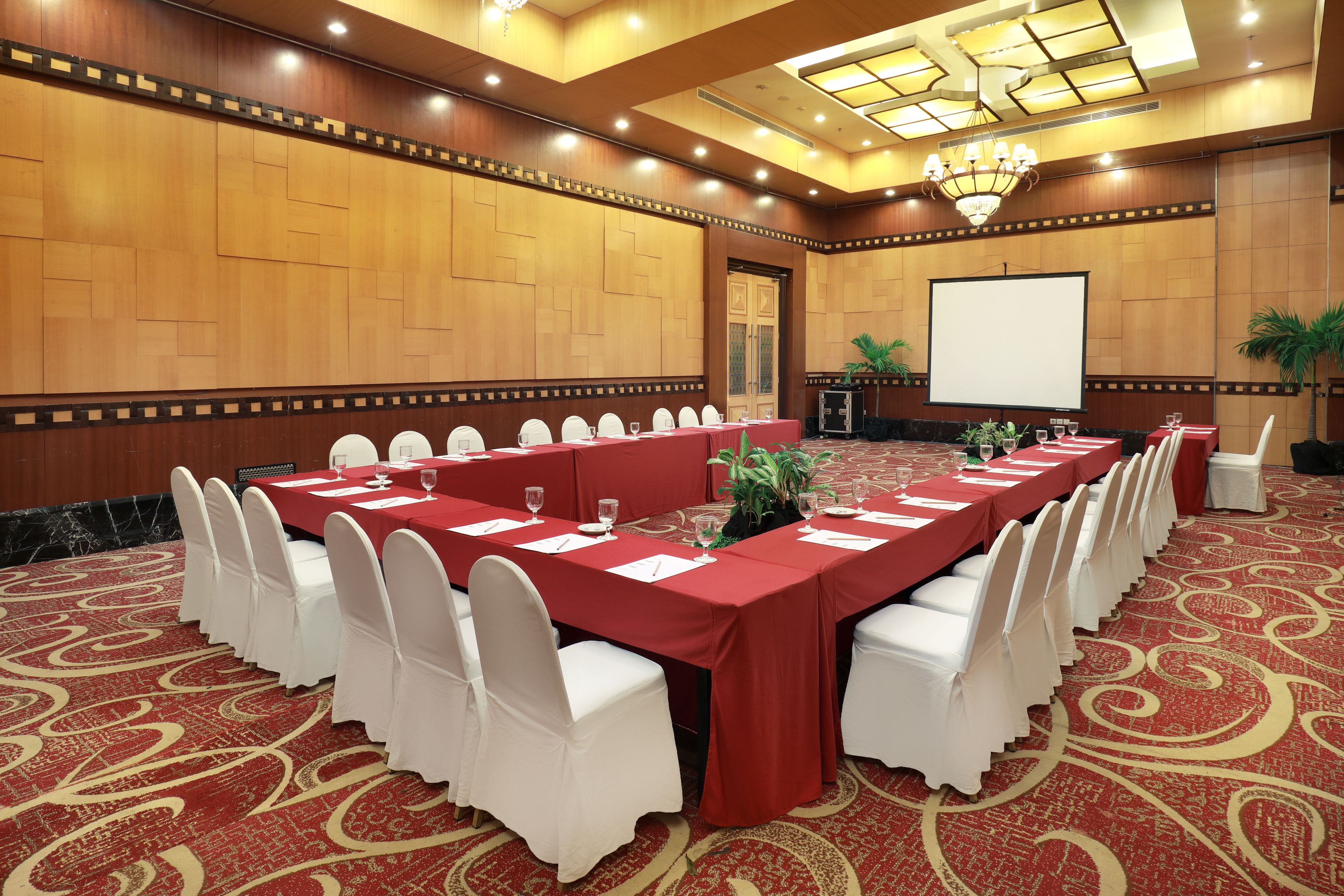 A conference room with a long table, white chairs, and a projector screen.