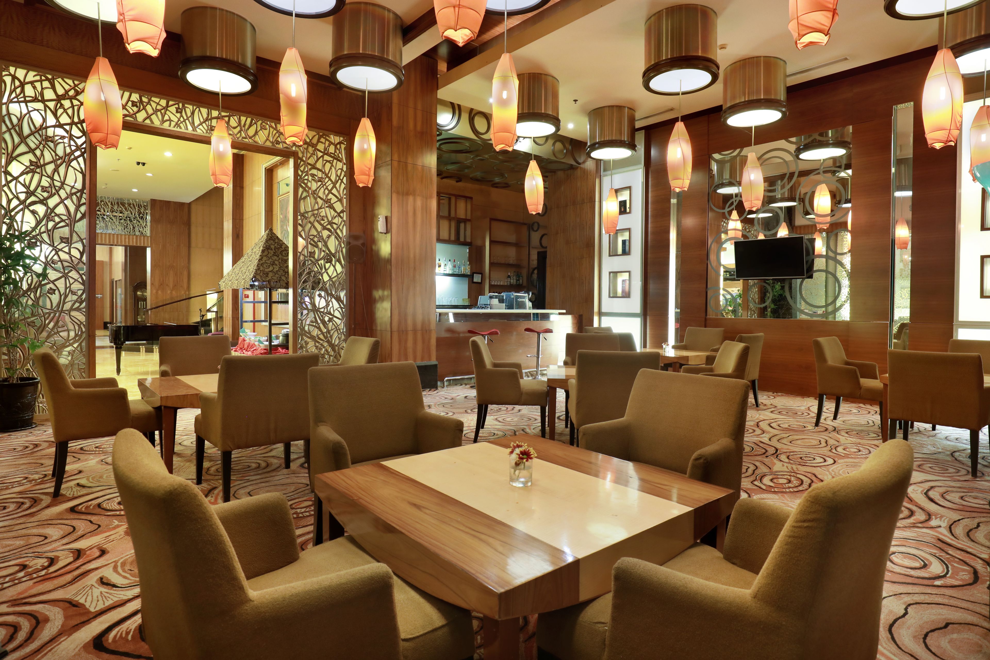 A hotel lobby with a wooden reception desk, multiple seating areas, and decorative hanging lights.
