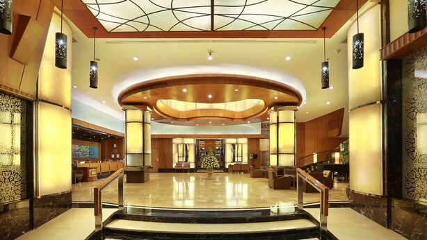 A spacious lobby with a marble floor, a central staircase, and a reception area with a Christmas tree.