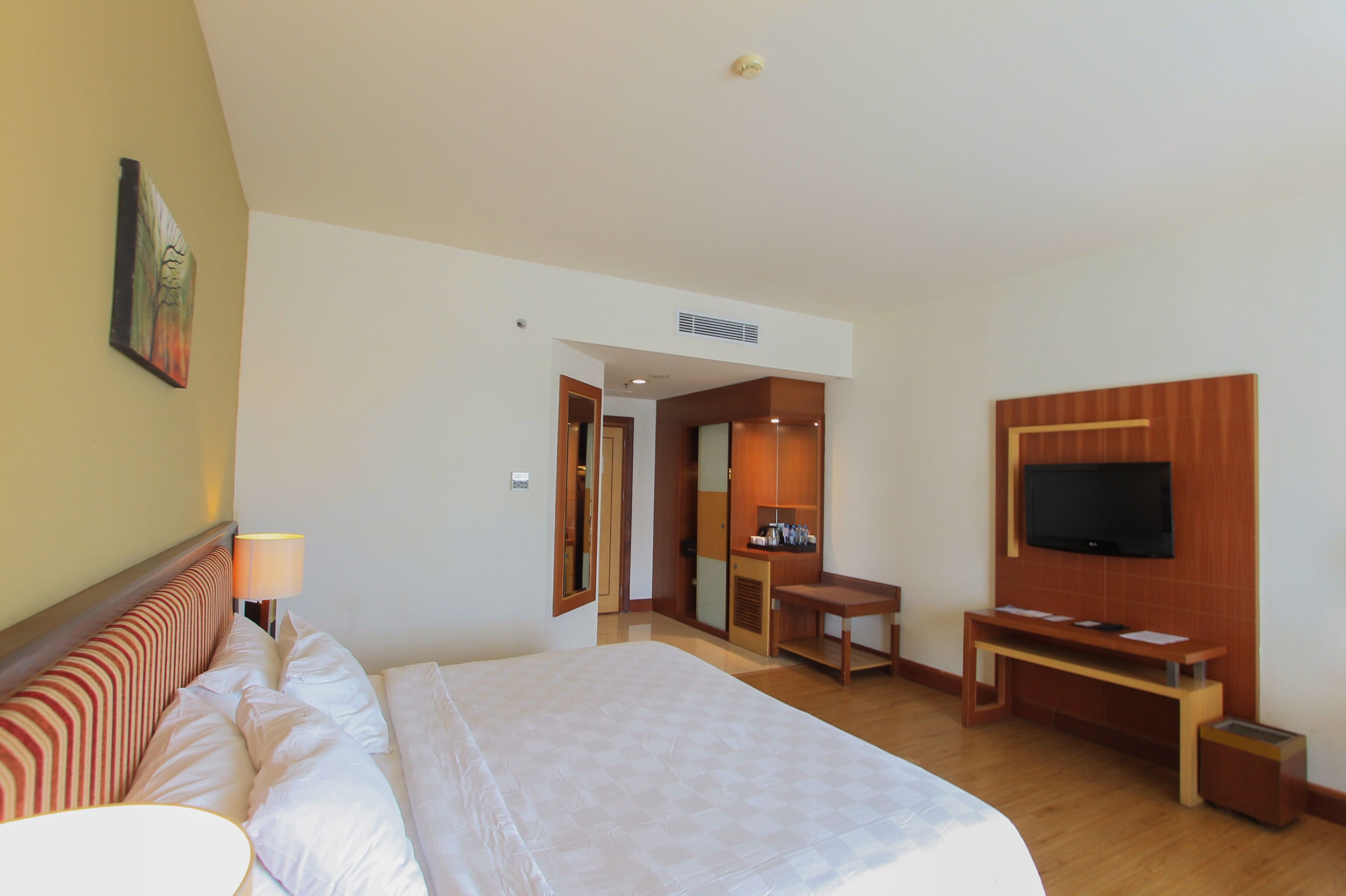 A hotel room with a bed, a desk, a television, and a bathroom visible through an open door.