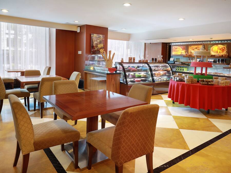 Un comedor con mesa y sillas de madera, un expositor de postres y un bufé con mantel rojo.