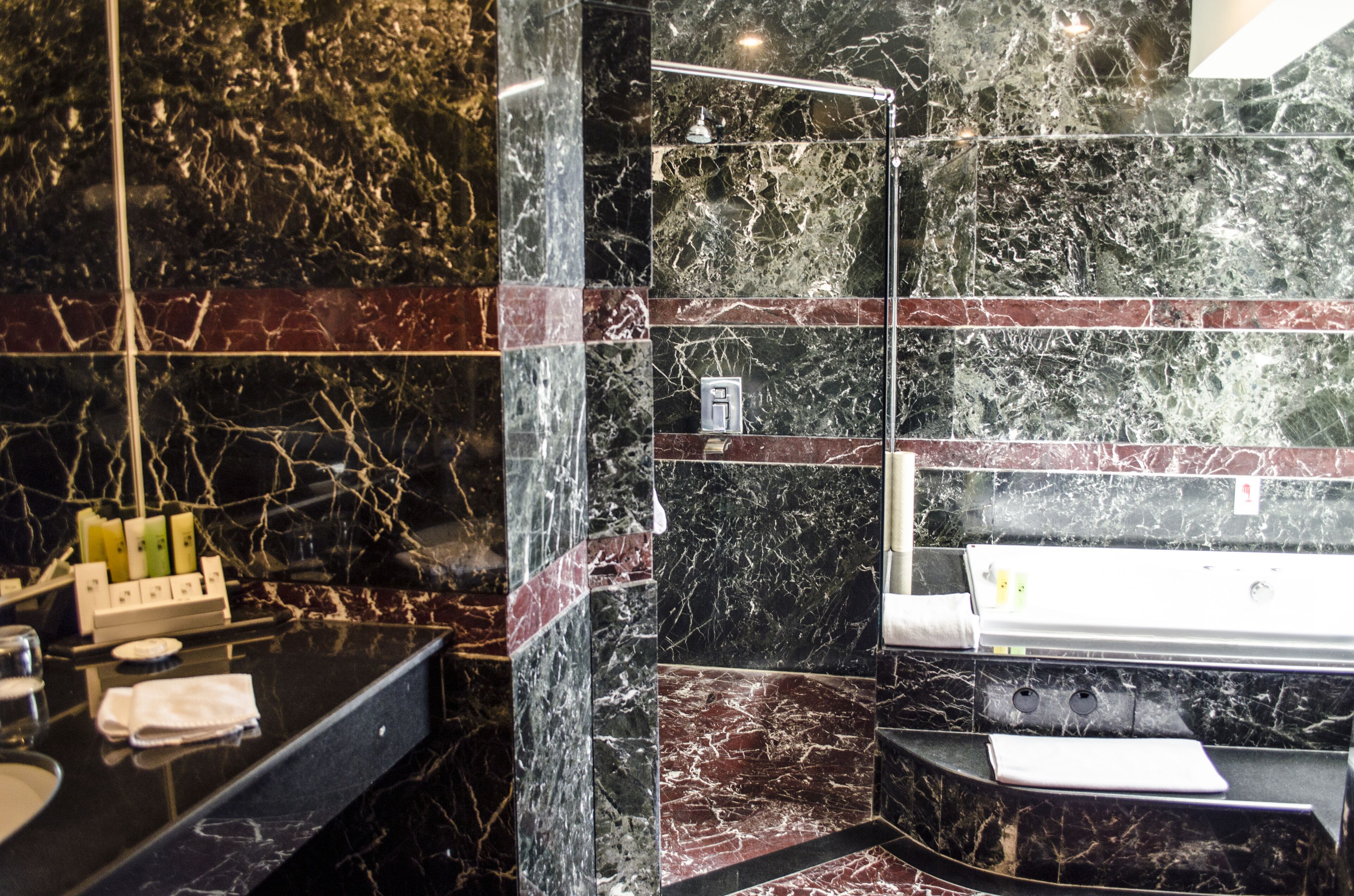 Un baño con un lavamanos de mármol negro, cabina de ducha de vidrio y pared revestida de mármol.