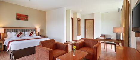 Habitación de hotel con cama, dos sofás, una mesa de centro, televisor y escritorio.