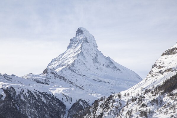 A snow-covered mountain peak with a sharp peak, surrounded by forested slopes and snow-covered valleys.