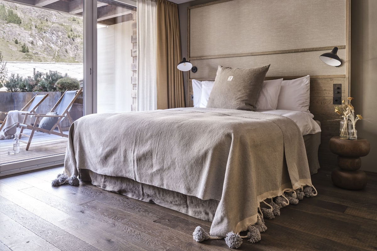 Quarto com cama, mesa de cabeceira, luminária e vista para o exterior.
