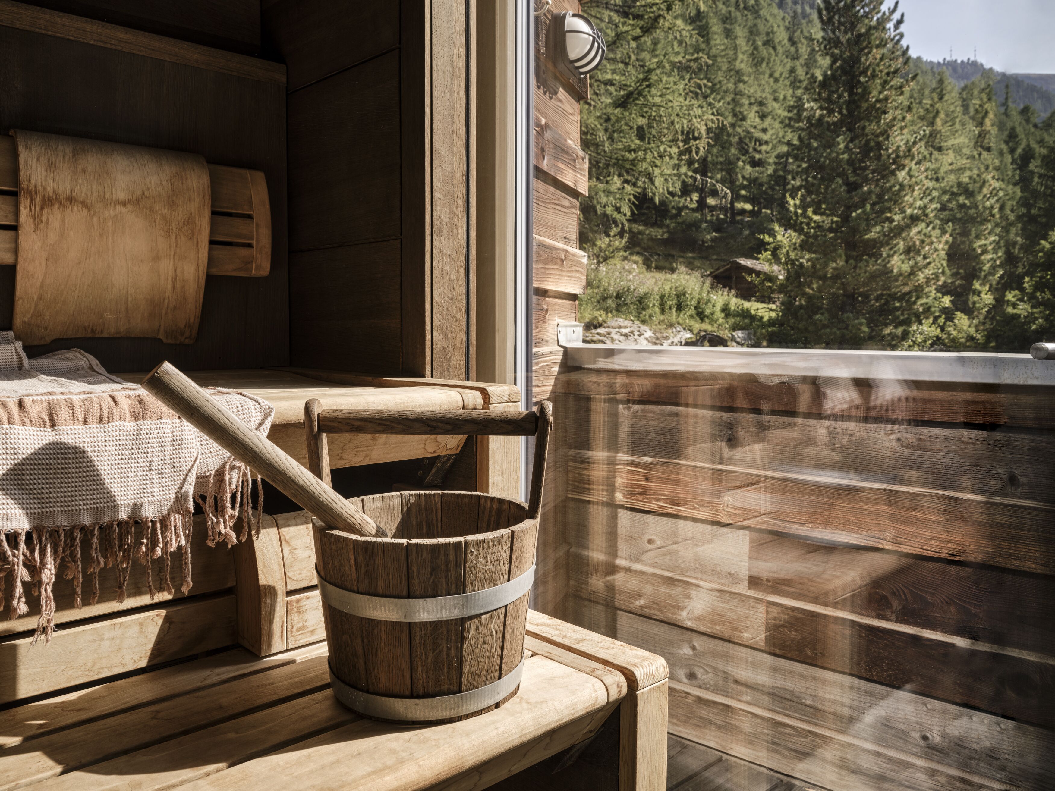 A wooden cabin interior with a rustic wooden bench, a woven rug, and a wooden bucket.