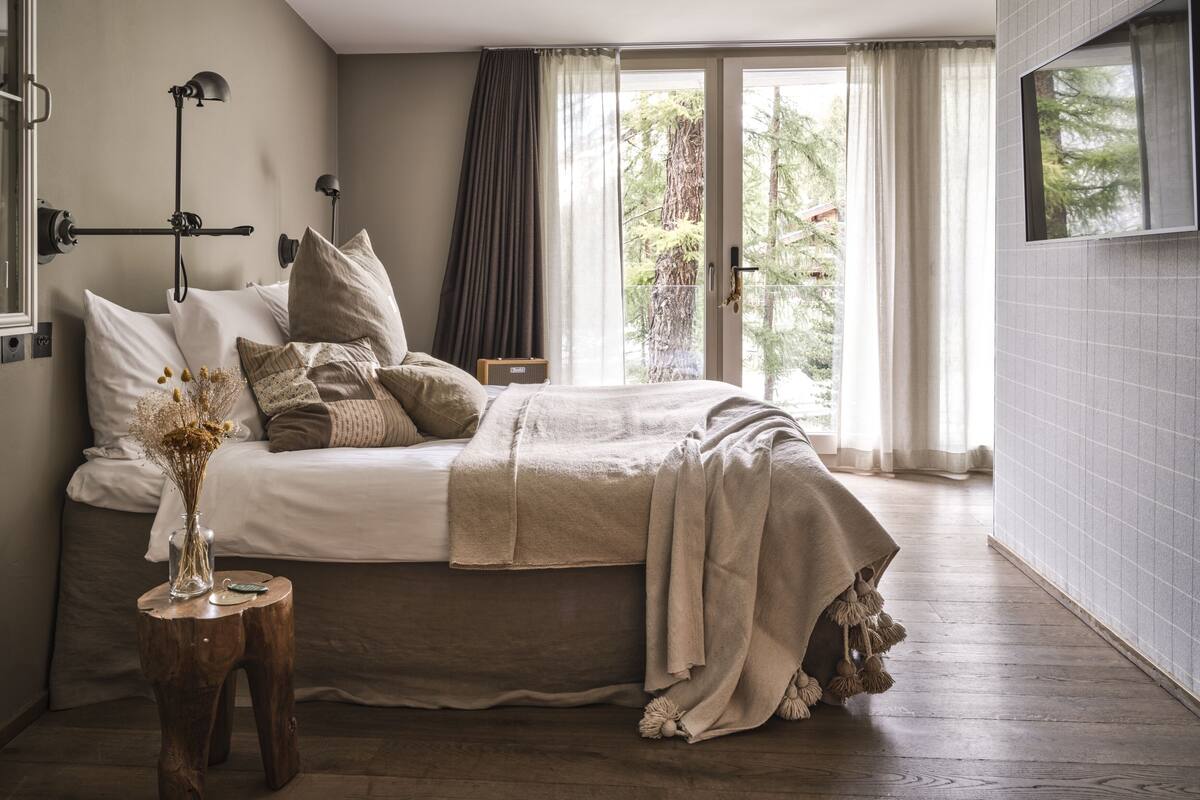 Quarto com cama grande, mesa de cabeceira com um vaso e vista para árvores pela janela.