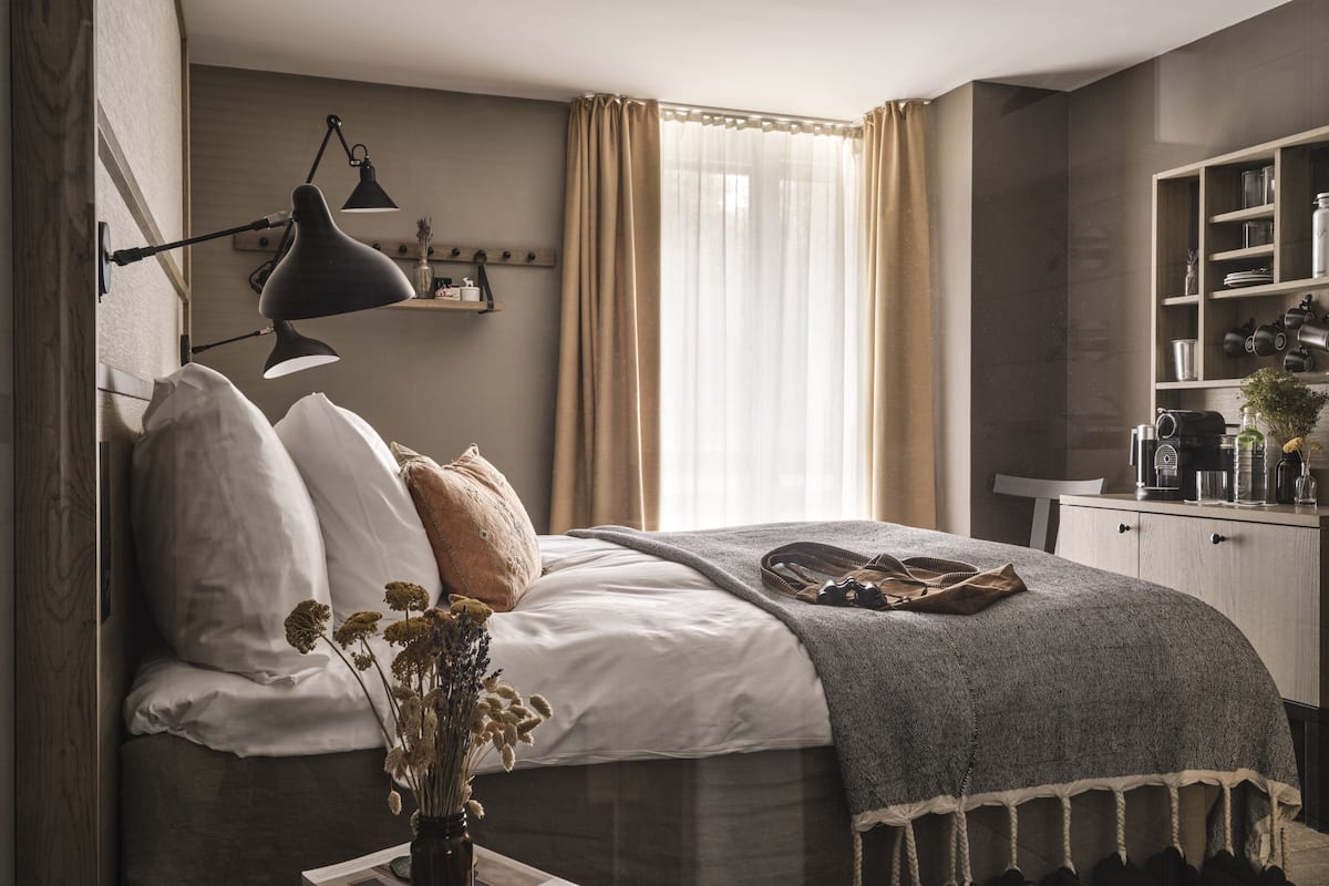 Um quarto com uma cama, uma mesa de cabeceira com um vaso, uma luminária e uma prateleira com artigos de higiene pessoal.