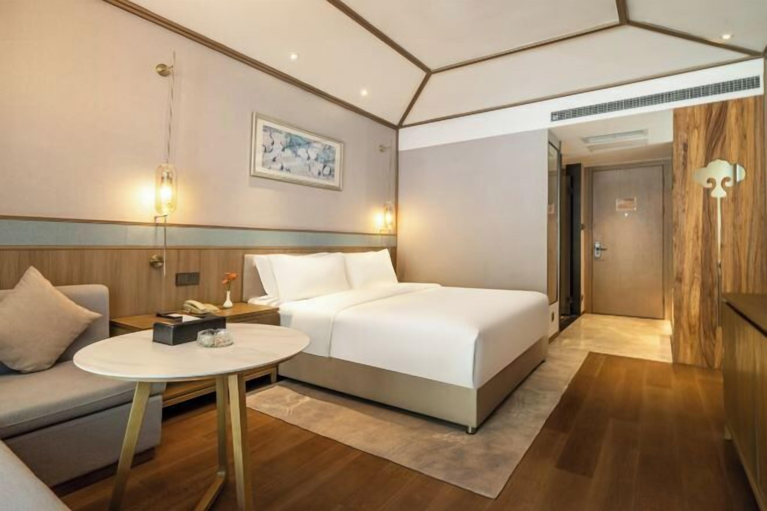 A modern hotel room with a large bed, a round table, and a sofa.