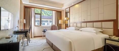 Habitación de hotel con una cama grande, un escritorio, una silla, un televisor y una ventana con cortinas.